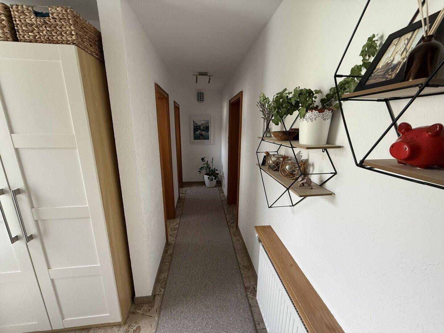 Langer Flur mit Teppichläufer, weißen Wänden und Holztüren.