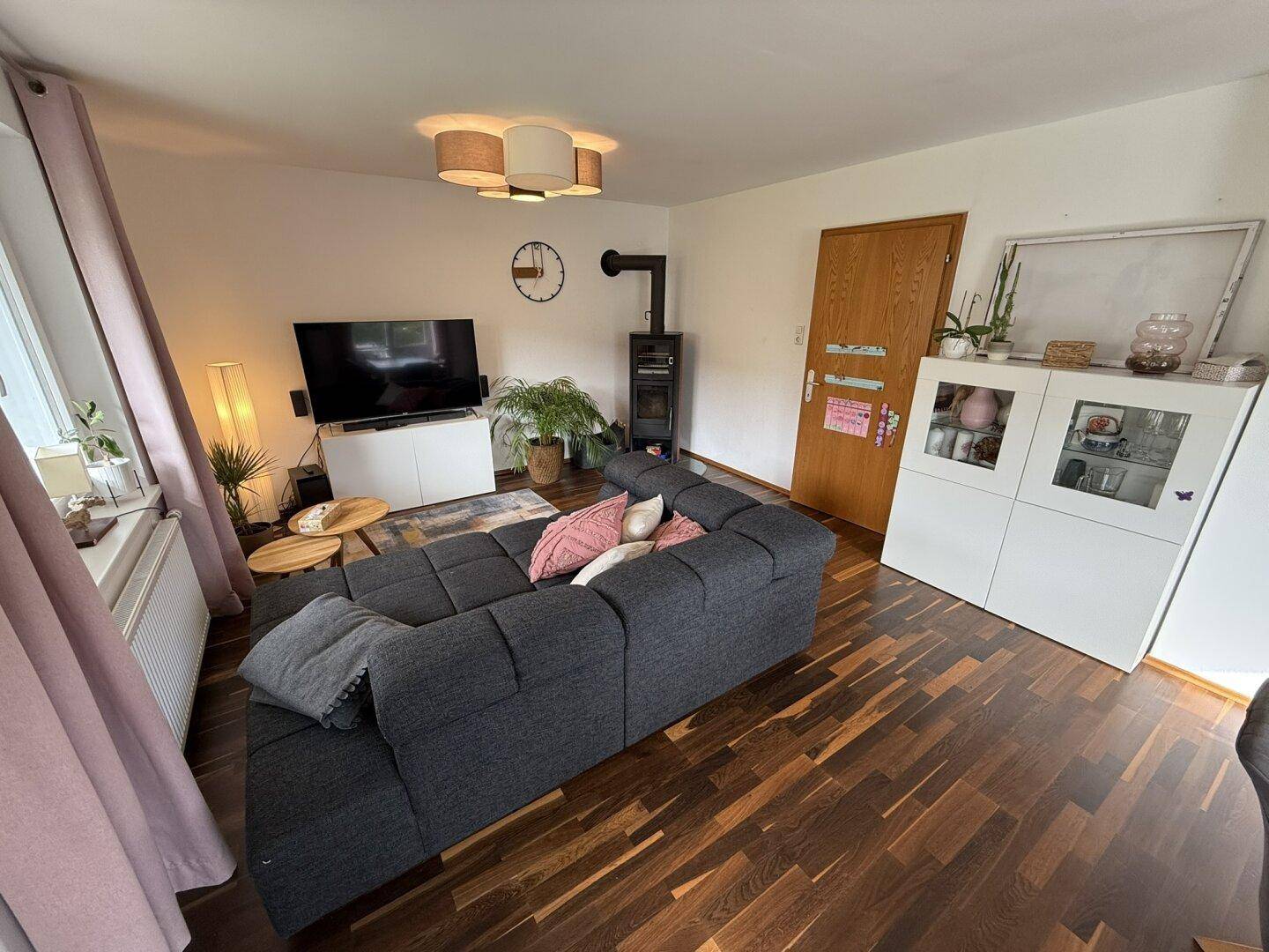 Gemütliches Wohnzimmer mit dunklem Holzboden, großem Sofa und einem Kaminofen.