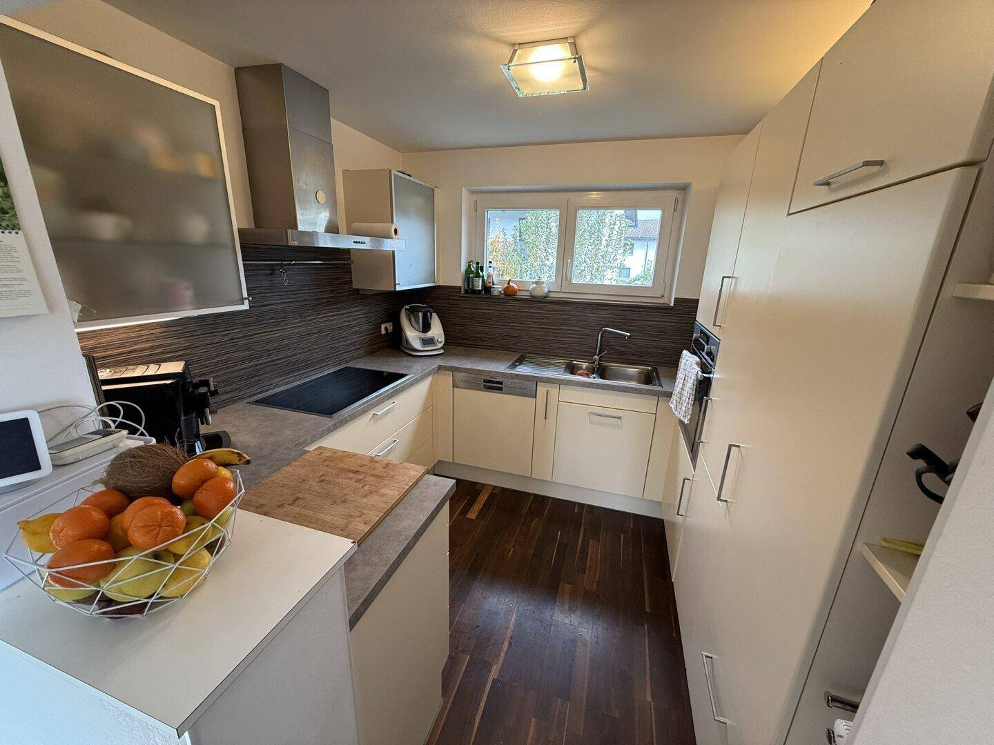 Funktionale Küche mit hellen Schränken, Einbaugeräten und Fenster mit Blick ins Grüne.