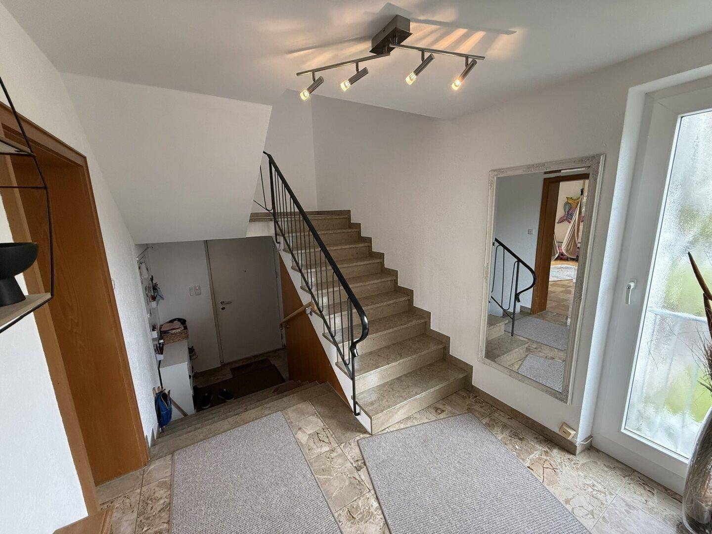 Heller Eingangsbereich mit Treppe, Fliesenboden und einem großen Spiegel.