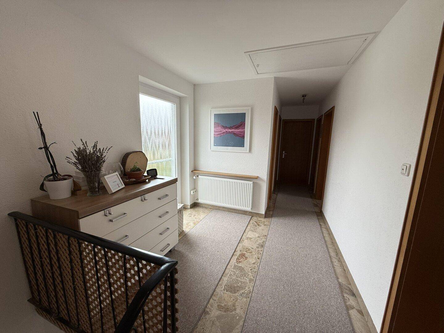 Oberer Flur mit Fliesenboden, Fenster und einer Kommode.