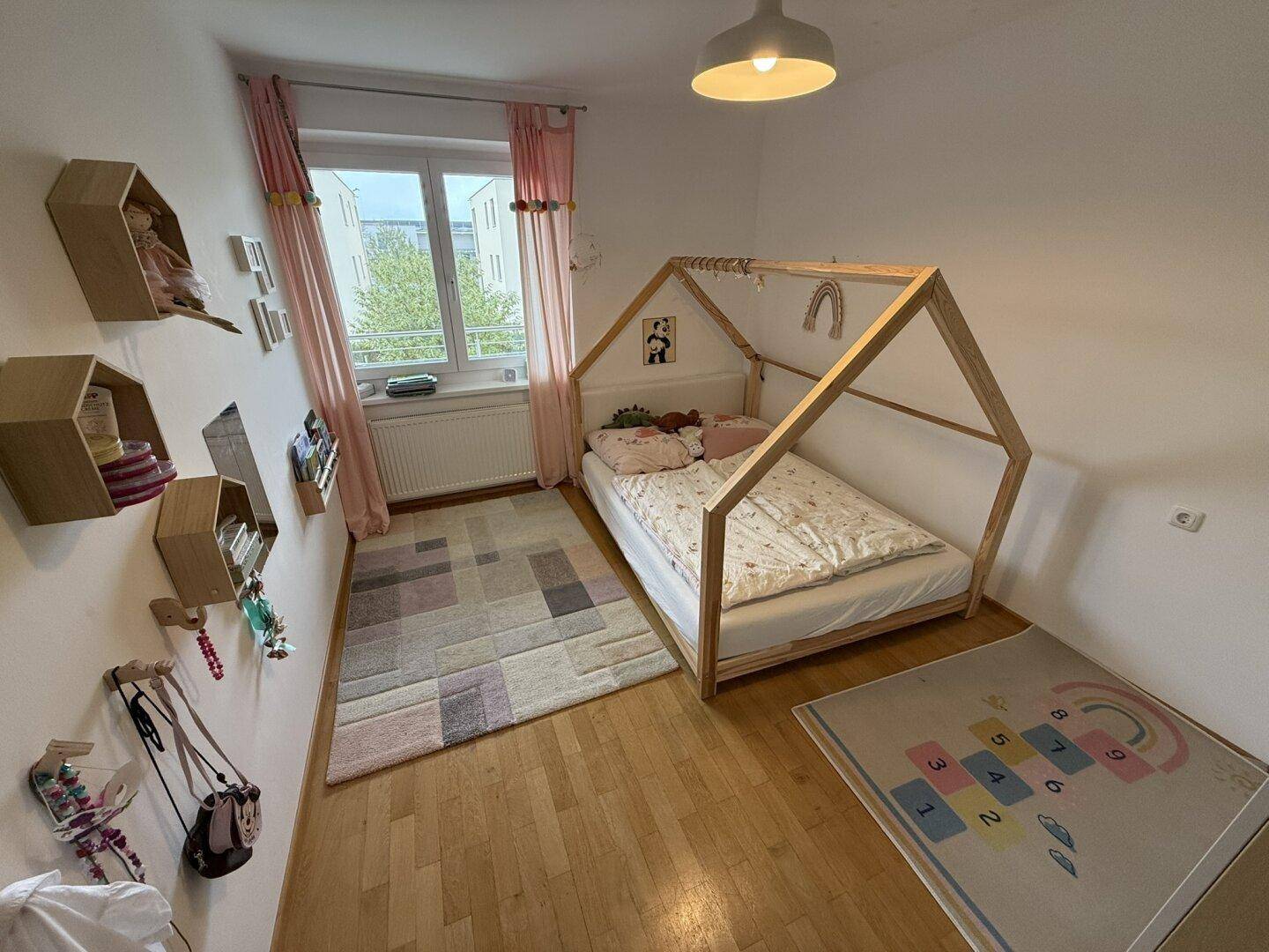 Freundliches Kinderzimmer mit Holzboden, Hausbett und bunten Teppichen.