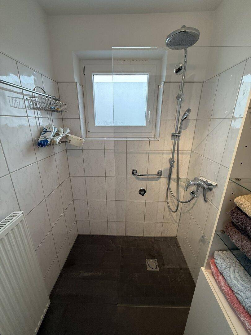 Modernes Duschbad mit weißen Fliesen, ebenerdiger Dusche und Fenster.