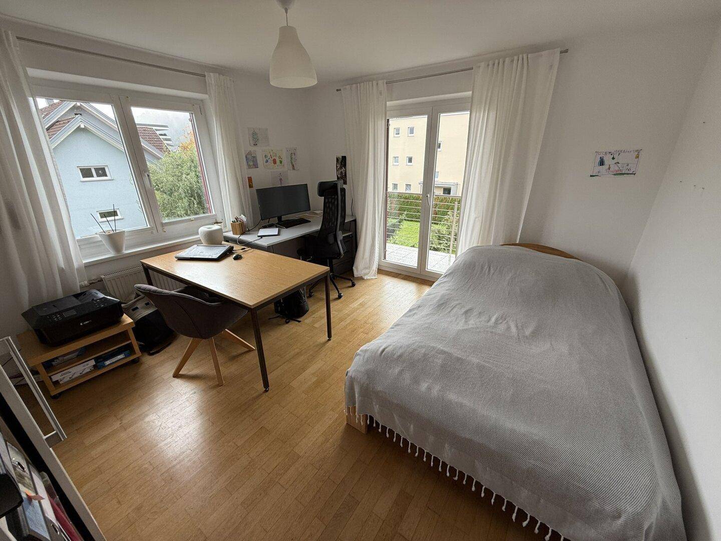 Helles Zimmer mit Holzboden, Schreibtisch und Zugang zu einem französischen Balkon.