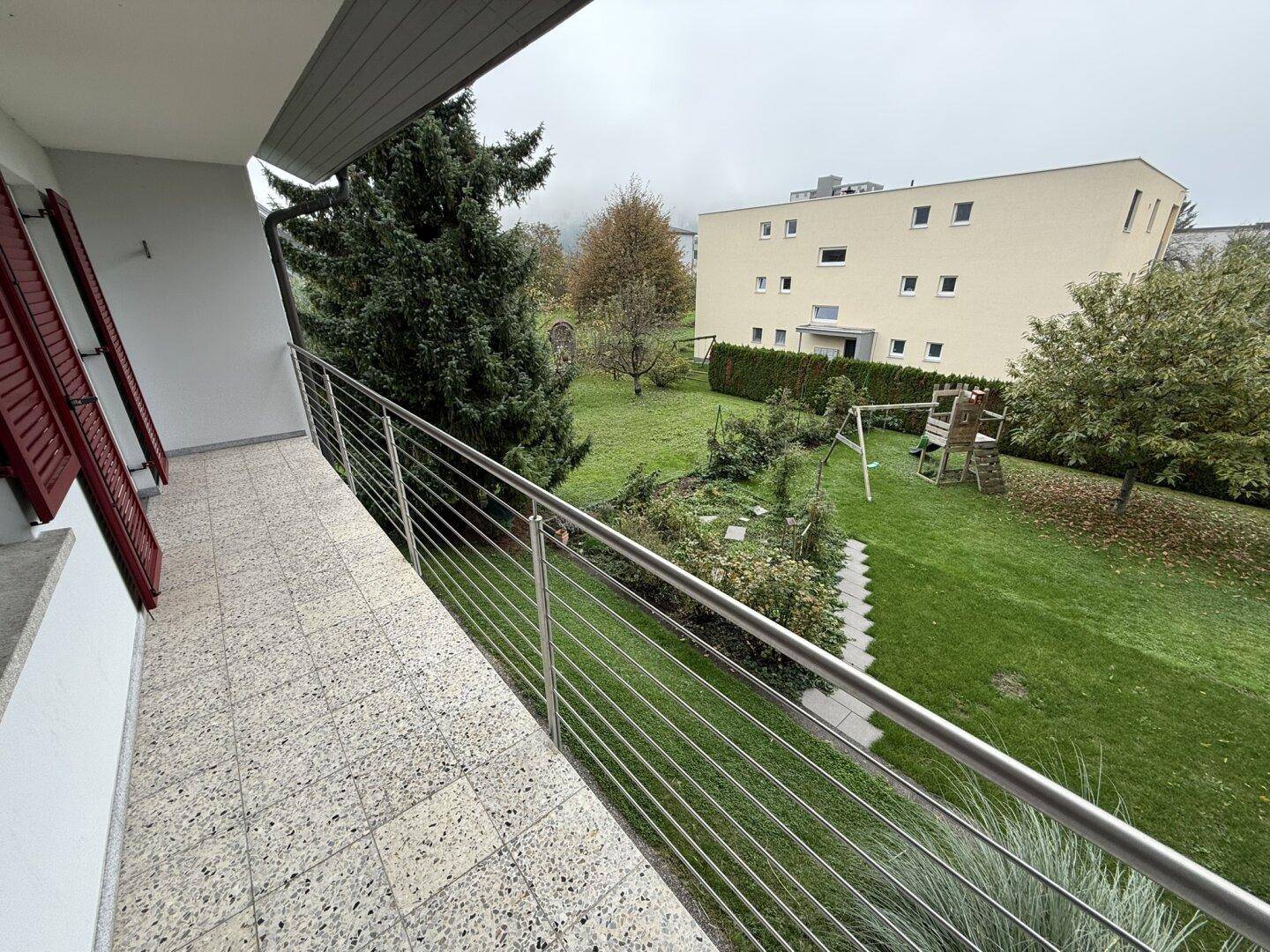 Heller Balkon mit Fliesenboden und Blick auf den grünen Garten und die Umgebung.