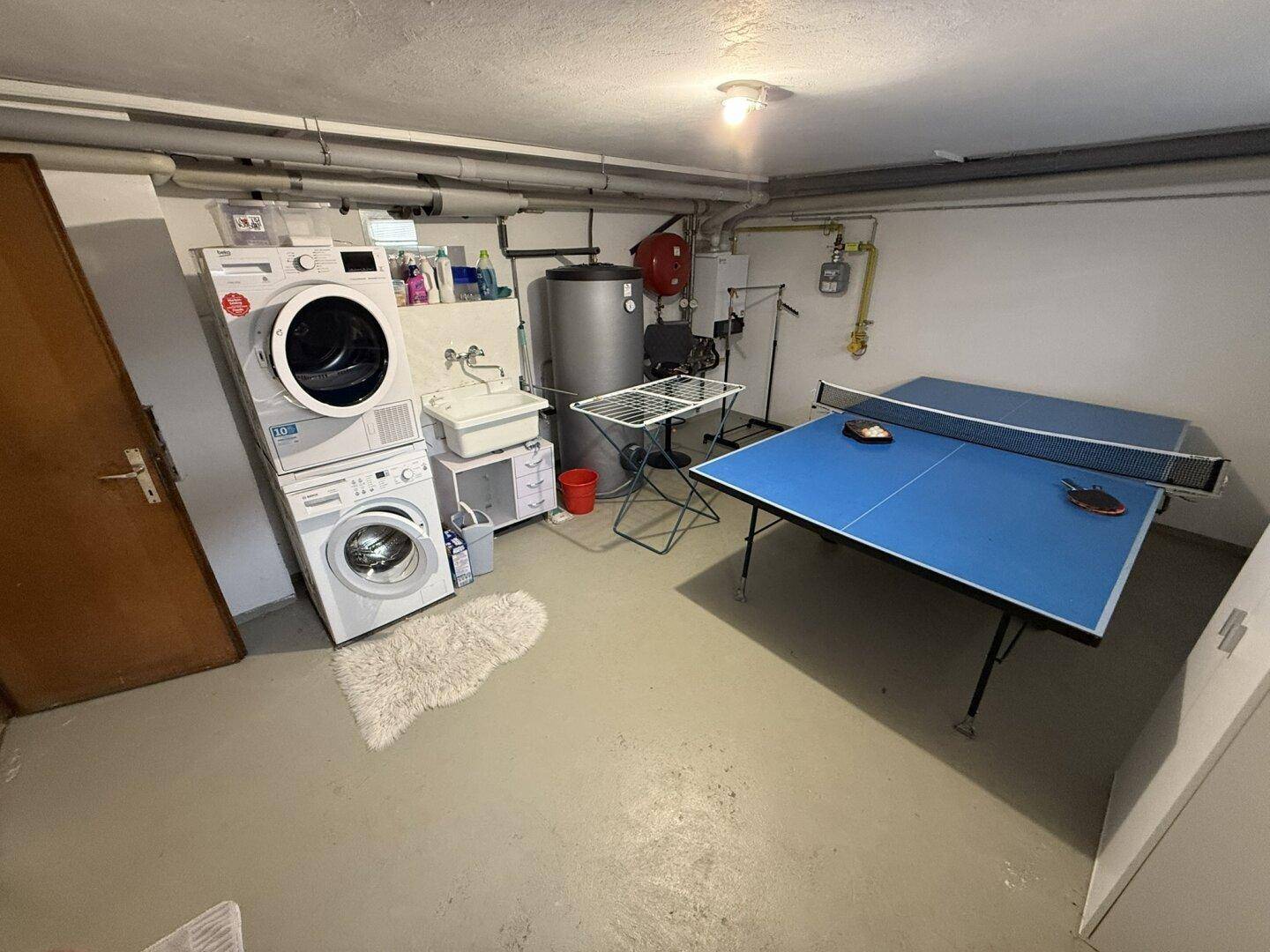 Geräumiger Hauswirtschaftsraum im Keller mit Waschmaschine, Trockner und Tischtennisplatte.