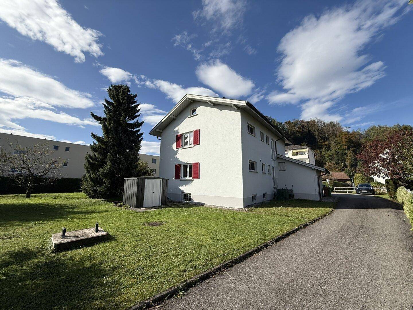 Seitenansicht des Hauses mit gepflegtem Rasen, einem Geräteschuppen und einer Zufahrt.