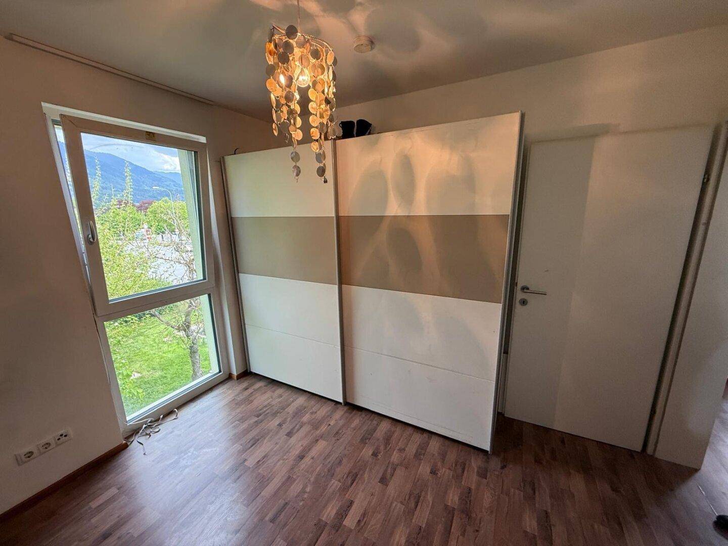 Schlafzimmer mit Laminatboden, großem Schiebetürenschrank und Fenster mit Grünblick.
