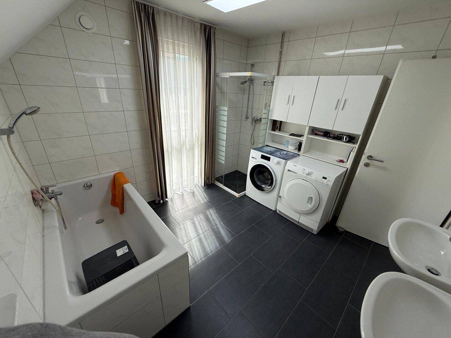 Badezimmer mit Badewanne, Duschkabine, Waschmaschine und Trockner unter Dachschräge.