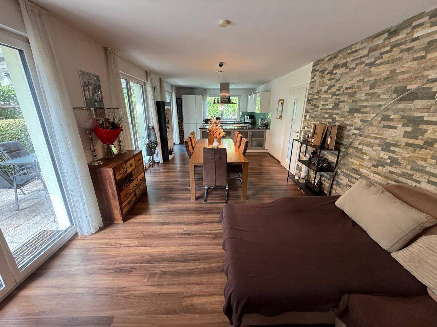 Geräumiger Wohn- und Essbereich mit Laminatboden, Steinwand und Zugang zur Terrasse.