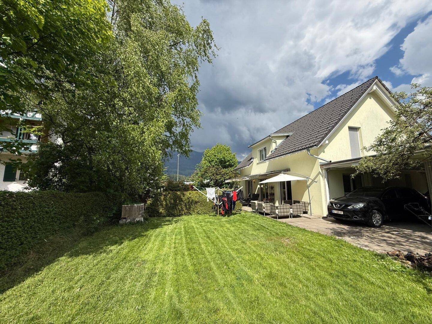 Weitläufiger Garten mit gepflegtem Rasen, Terrasse und Blick auf die umliegende Berglandschaft.