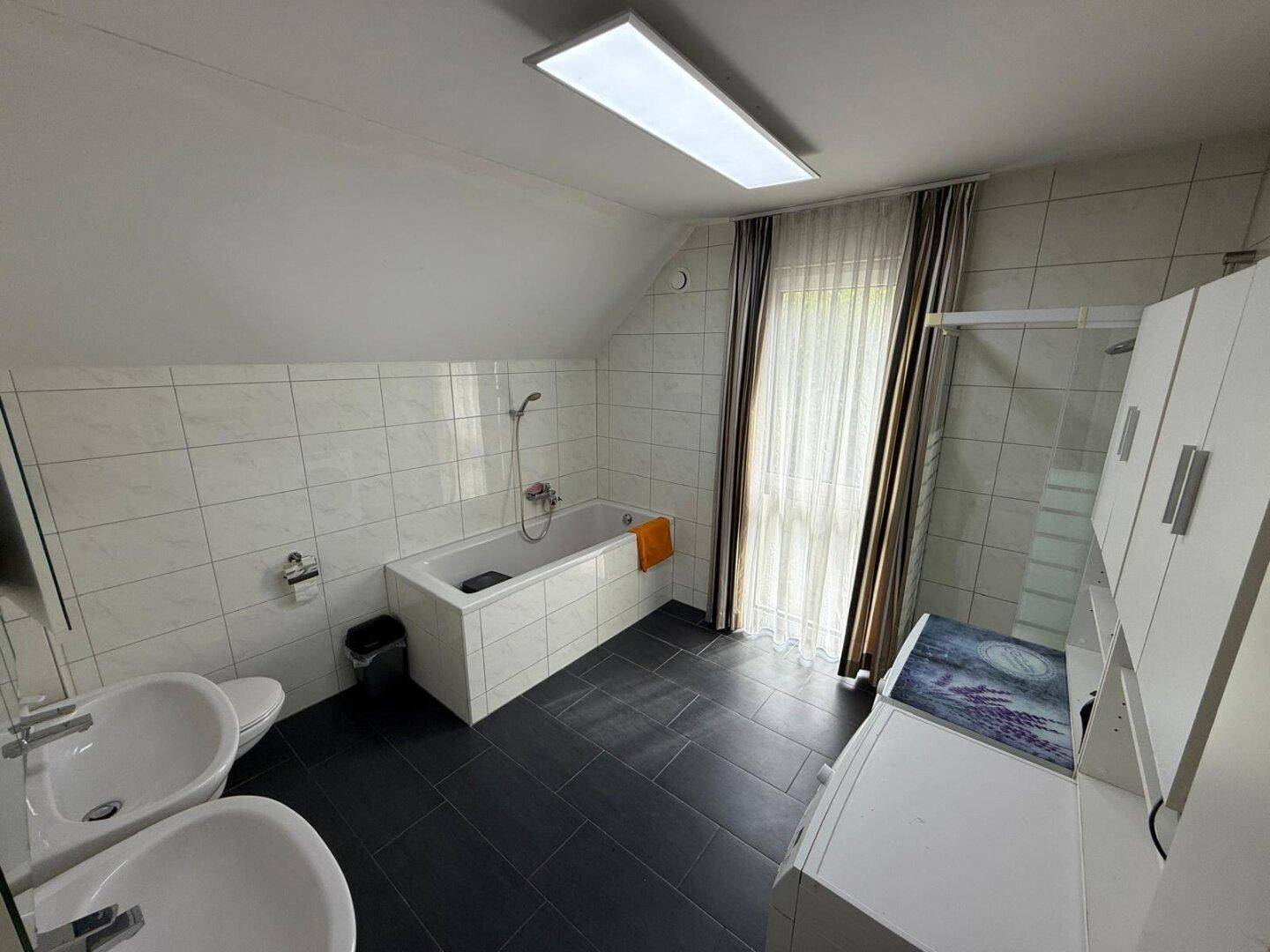 Geräumiges Badezimmer mit Badewanne, Doppelwaschbecken und WC unter der Dachschräge.