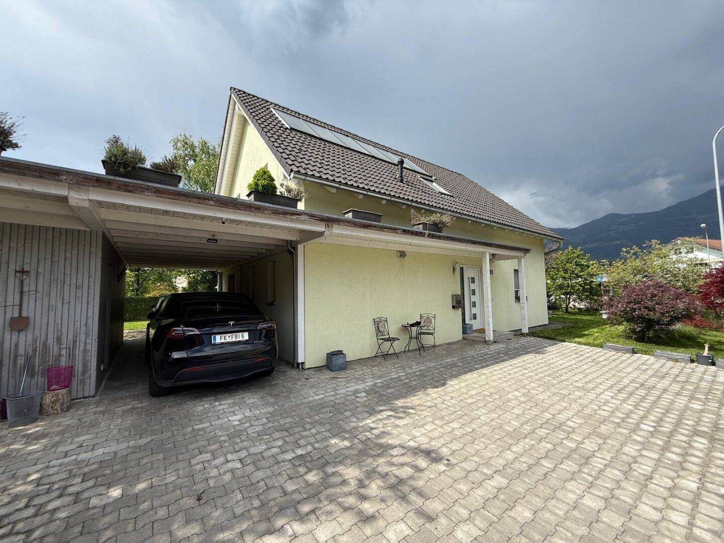 Vorderansicht des Hauses mit gepflasterter Einfahrt, Carport und Solaranlage auf dem Dach.