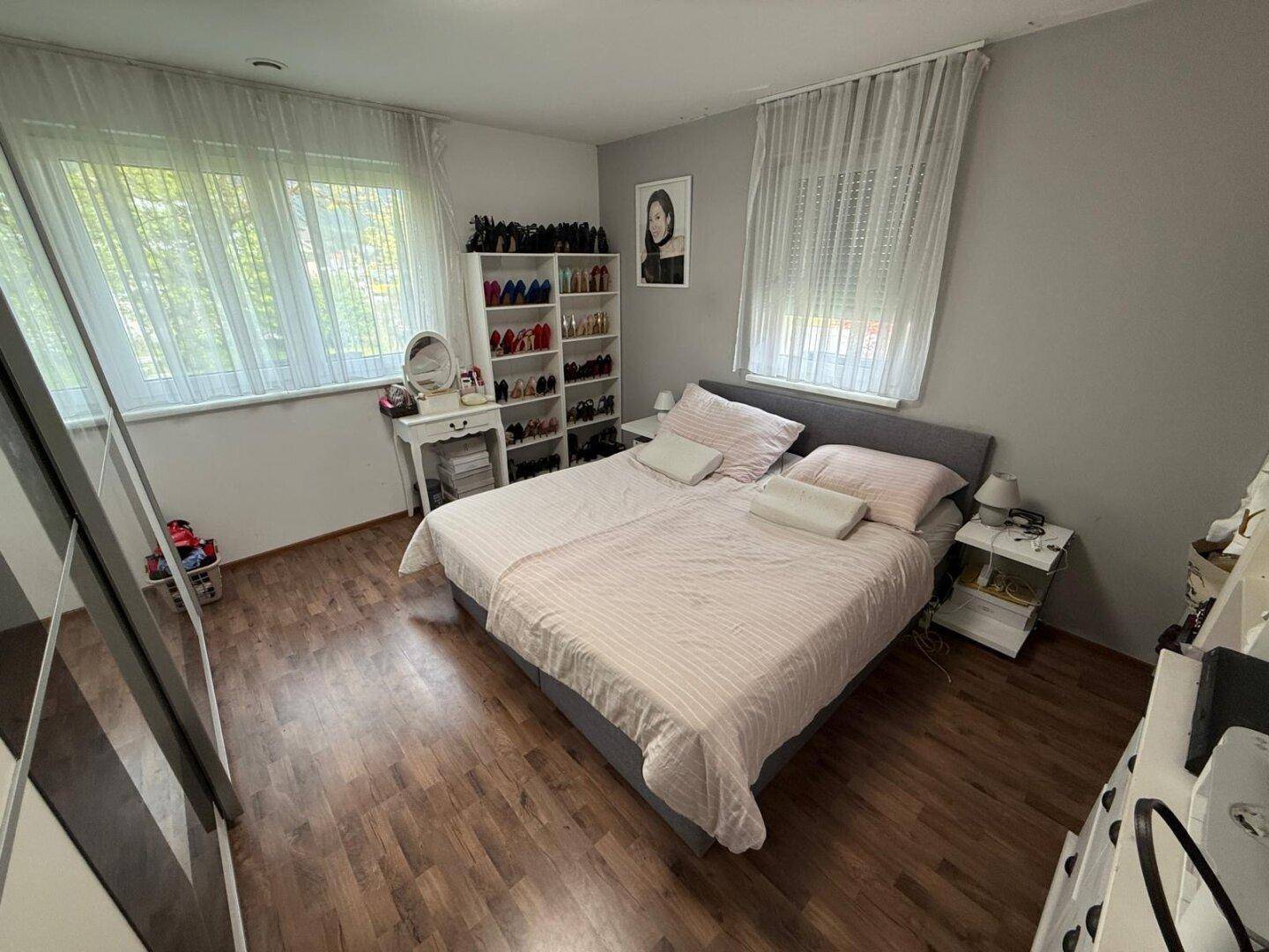 Helles Schlafzimmer mit Doppelbett, Laminatboden und zwei großen Fenstern.