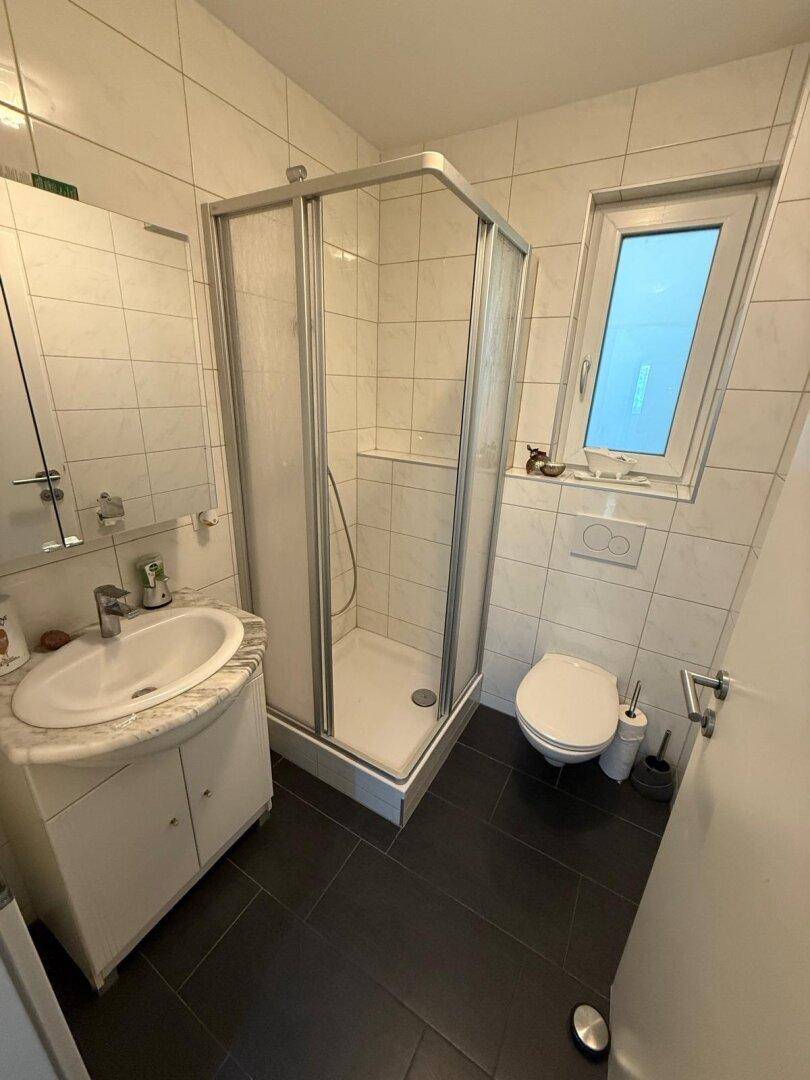Modernes Badezimmer mit Duschkabine, Waschbecken, WC und Fenster.