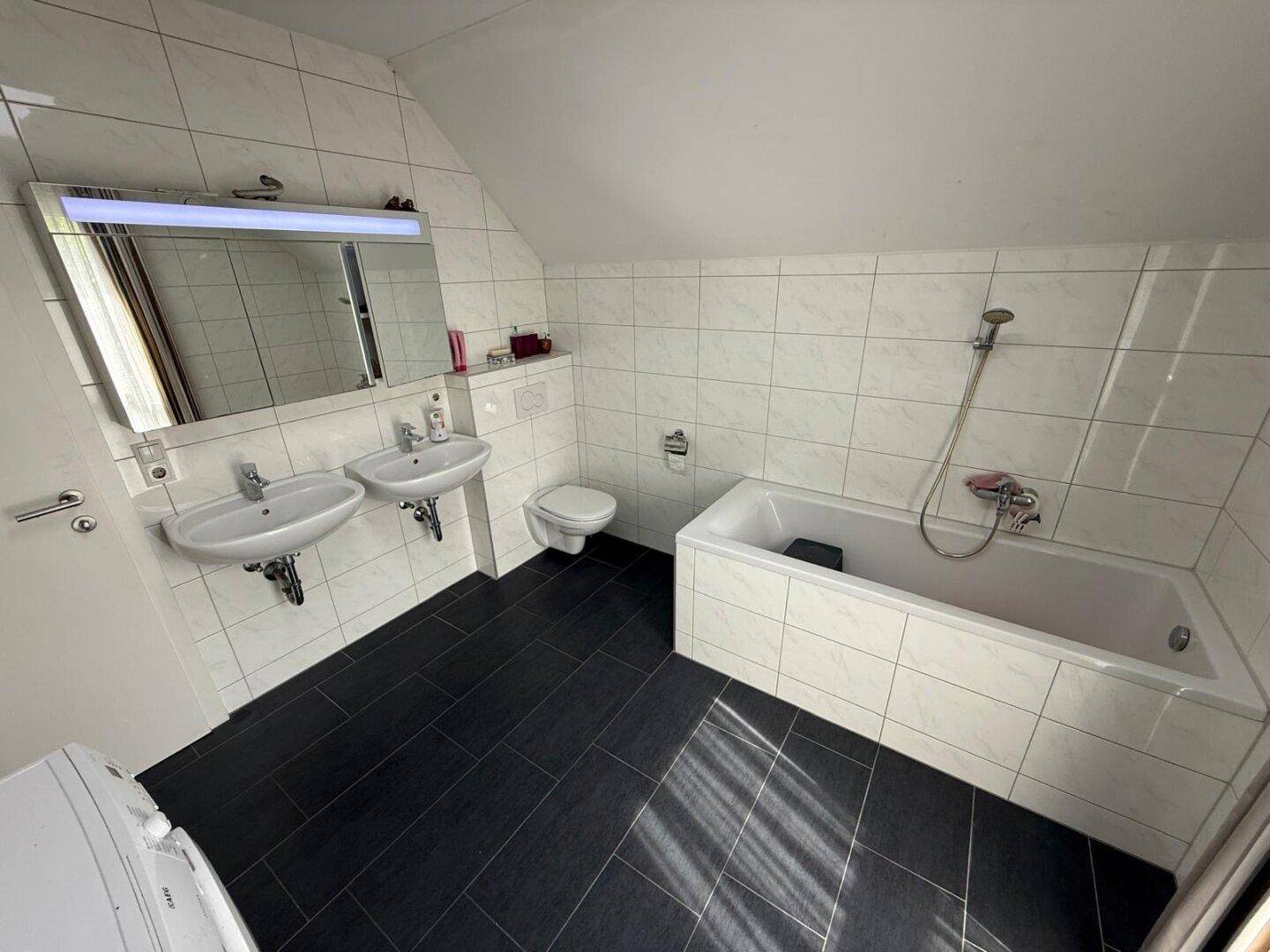 Badezimmer mit Badewanne, Doppelwaschbecken, WC und Fliesenboden unter Dachschräge.
