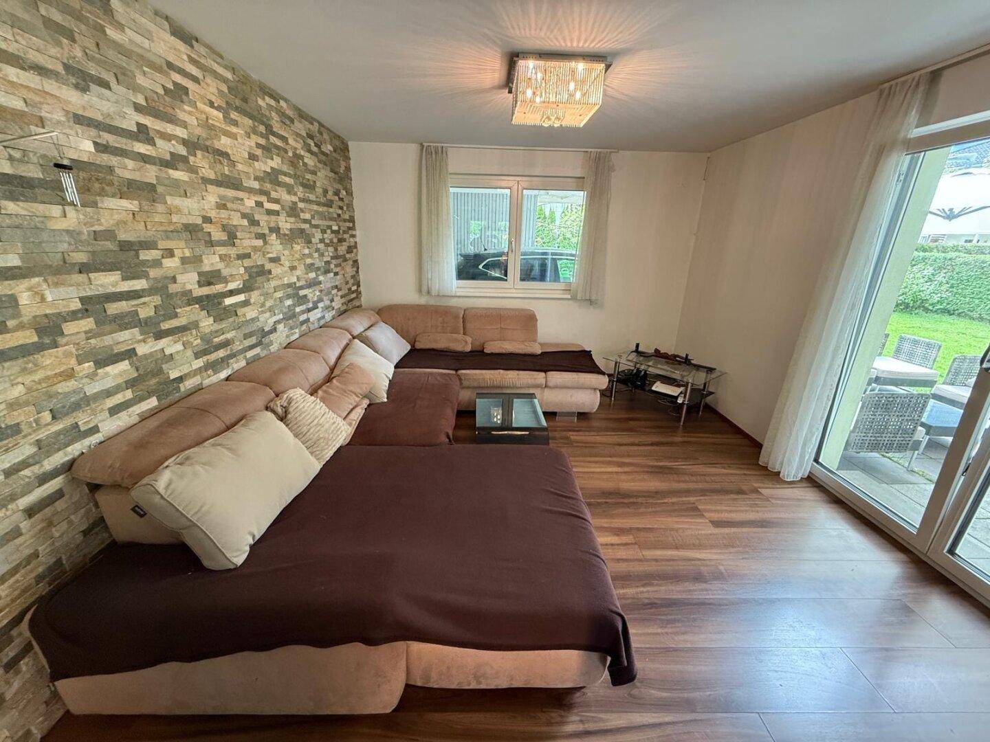 Geräumiges Wohnzimmer mit großer Eckcouch, Laminatboden und Zugang zur Terrasse.