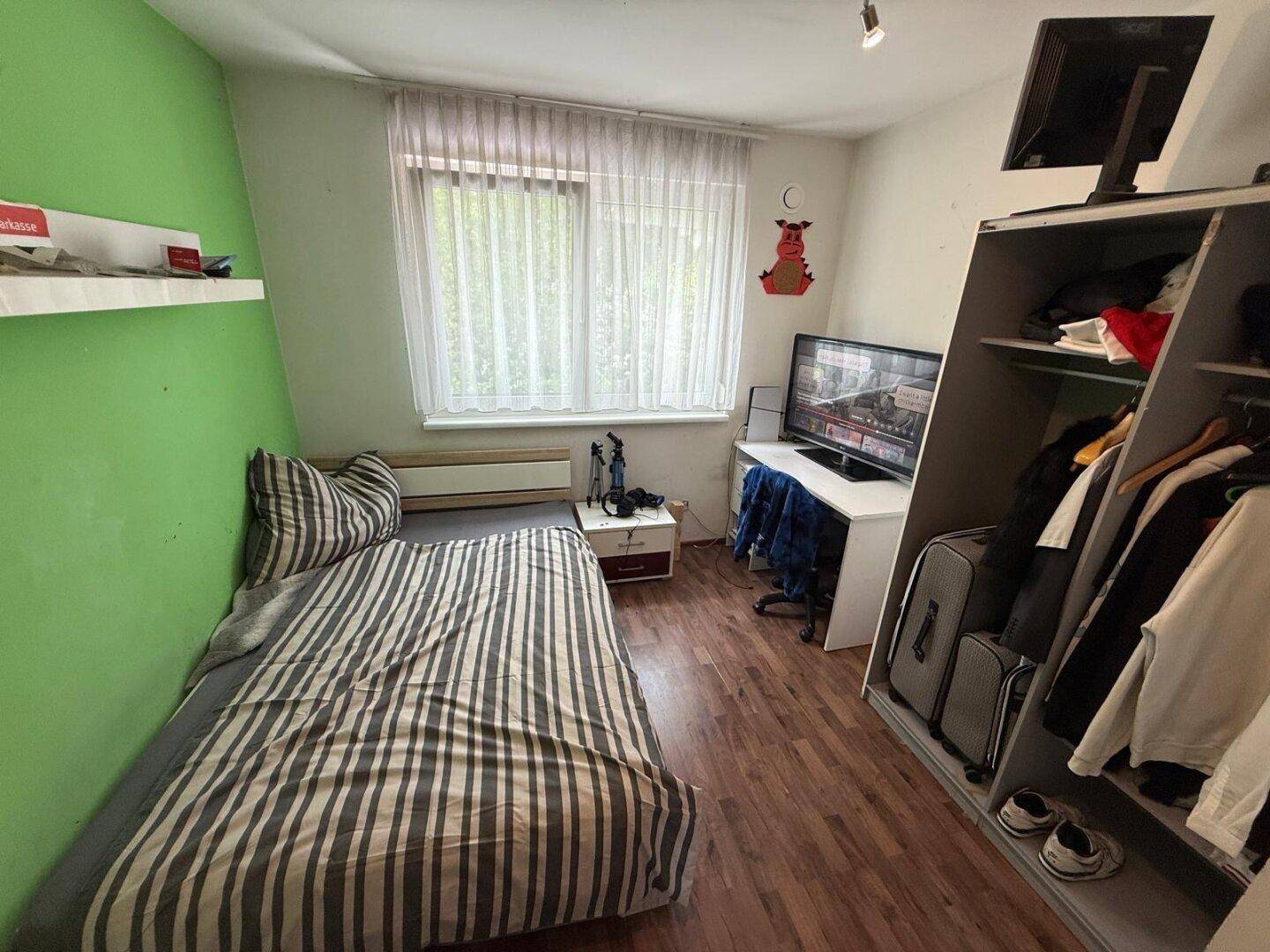 Helles Schlafzimmer mit grün gestrichener Wand, Holzboden und Einzelbett.