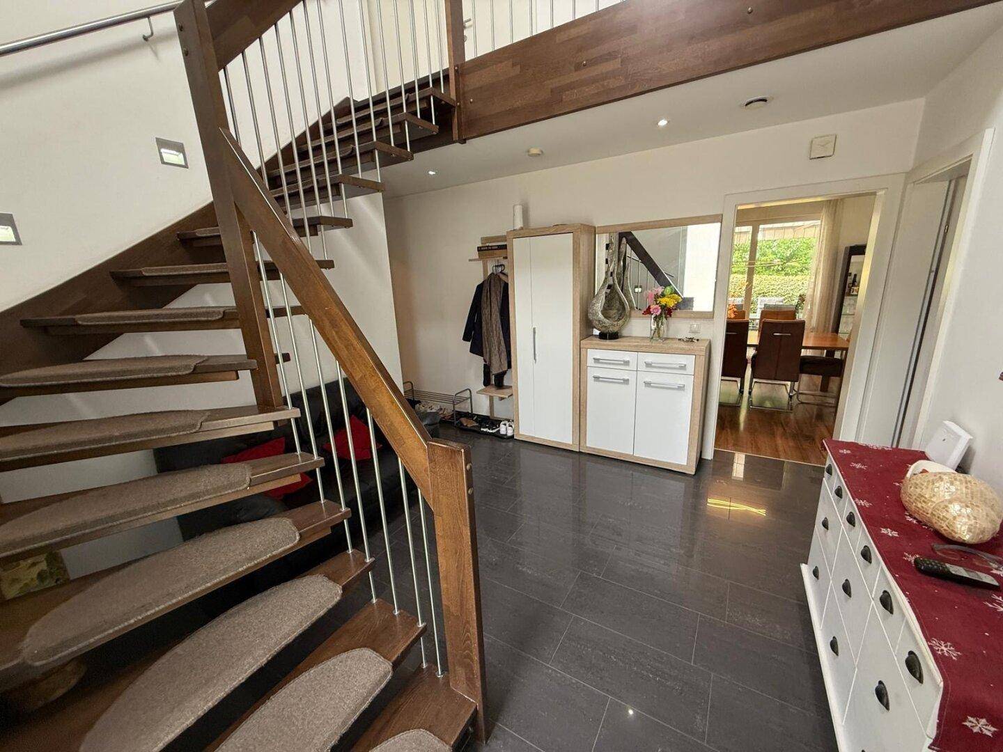 Geräumiger Eingangsbereich mit dunklen Fliesen, Holztreppe und Garderobe.