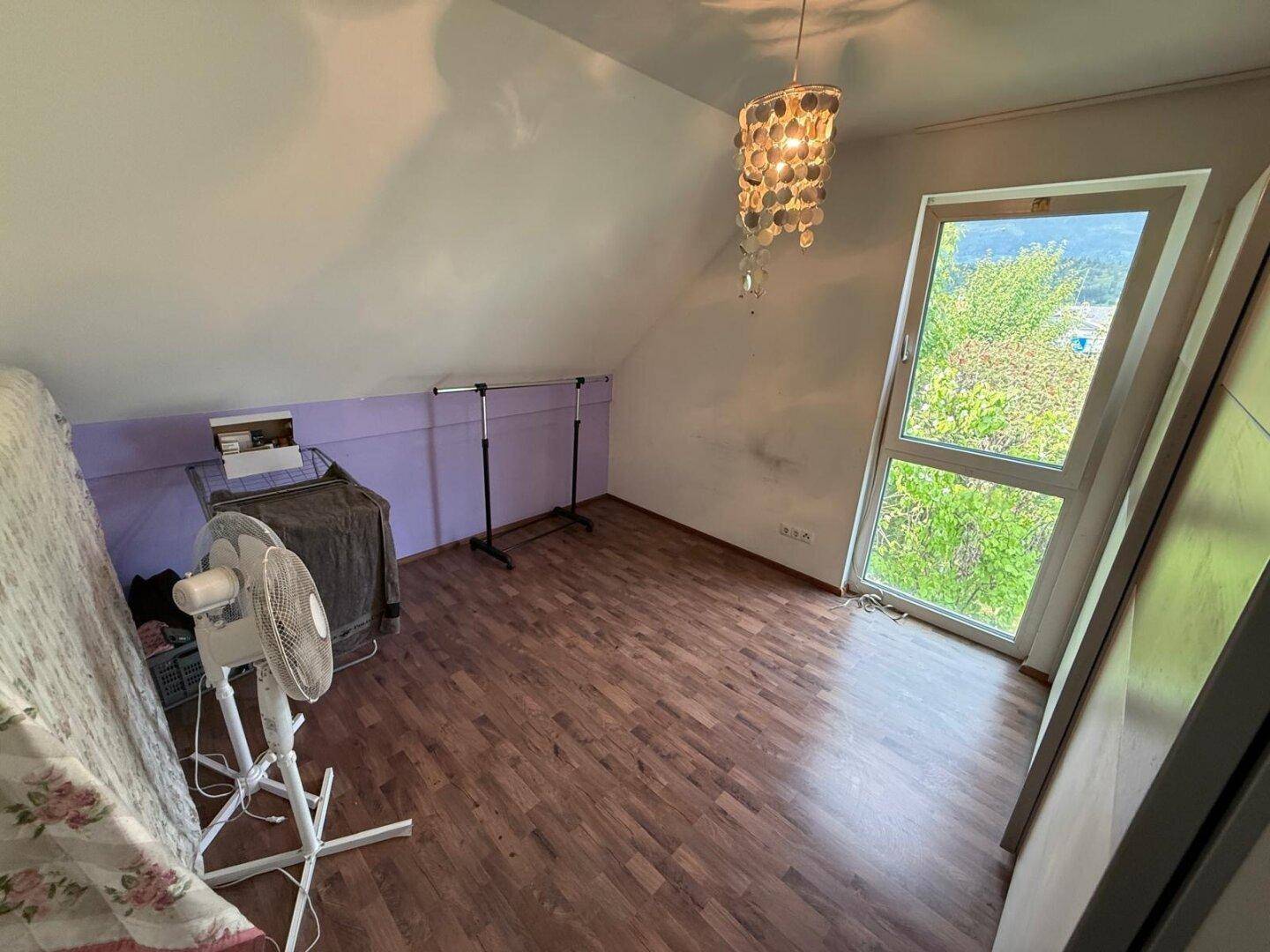 Dachgeschosszimmer mit schrägen Wänden, Holzboden und großem Fenster.