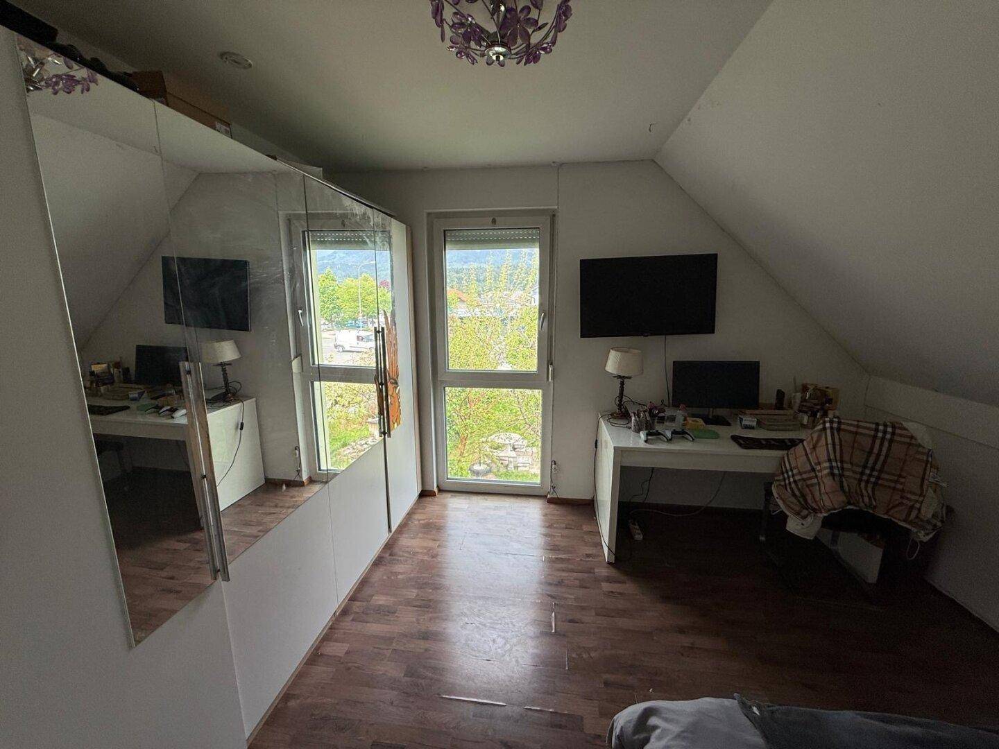 Dachgeschosszimmer mit Spiegelschrank, Holzboden und Fenster mit Ausblick.