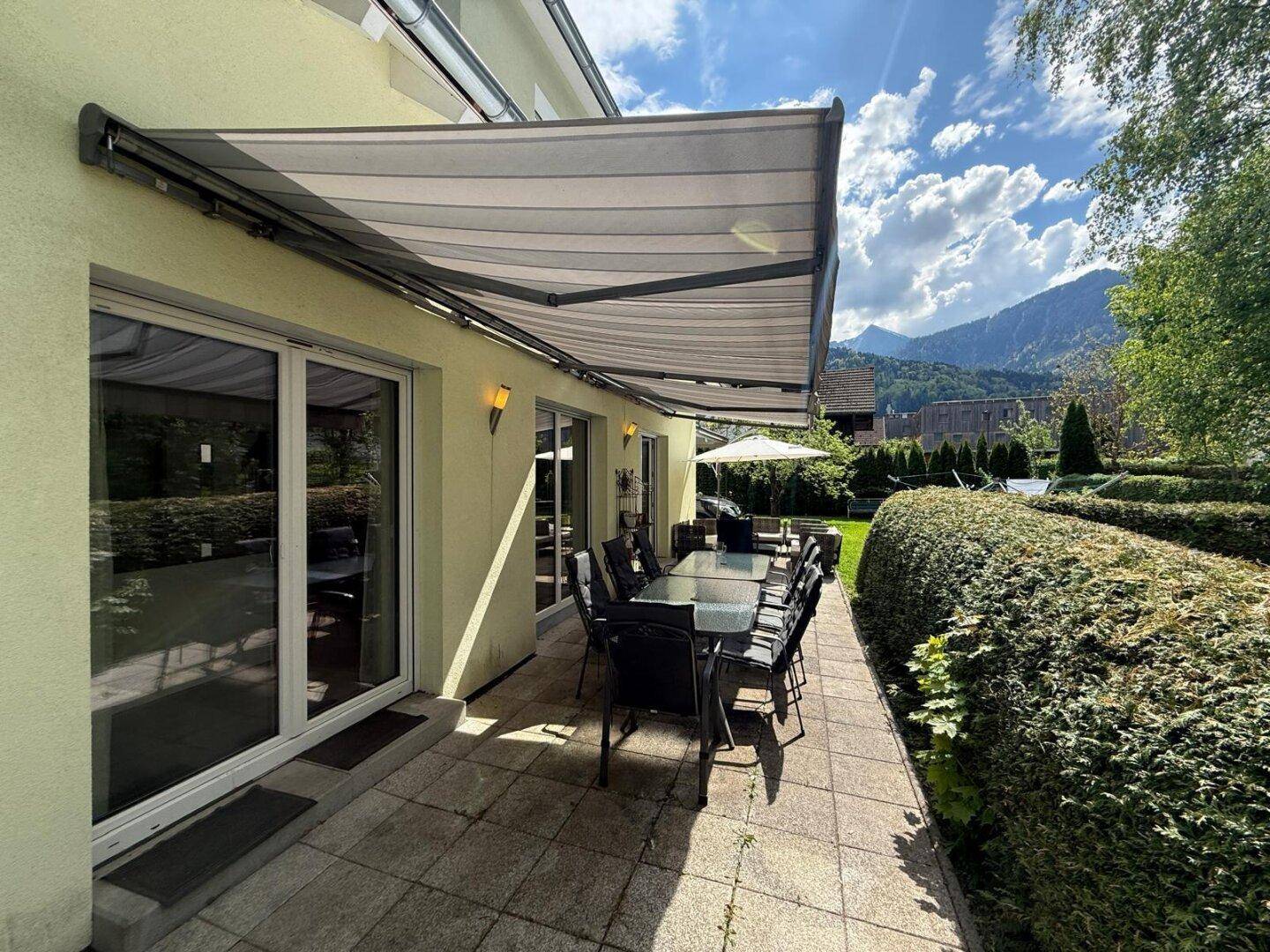 Geräumige Terrasse mit großem Esstisch, Markise und weitem Blick auf die Berge.