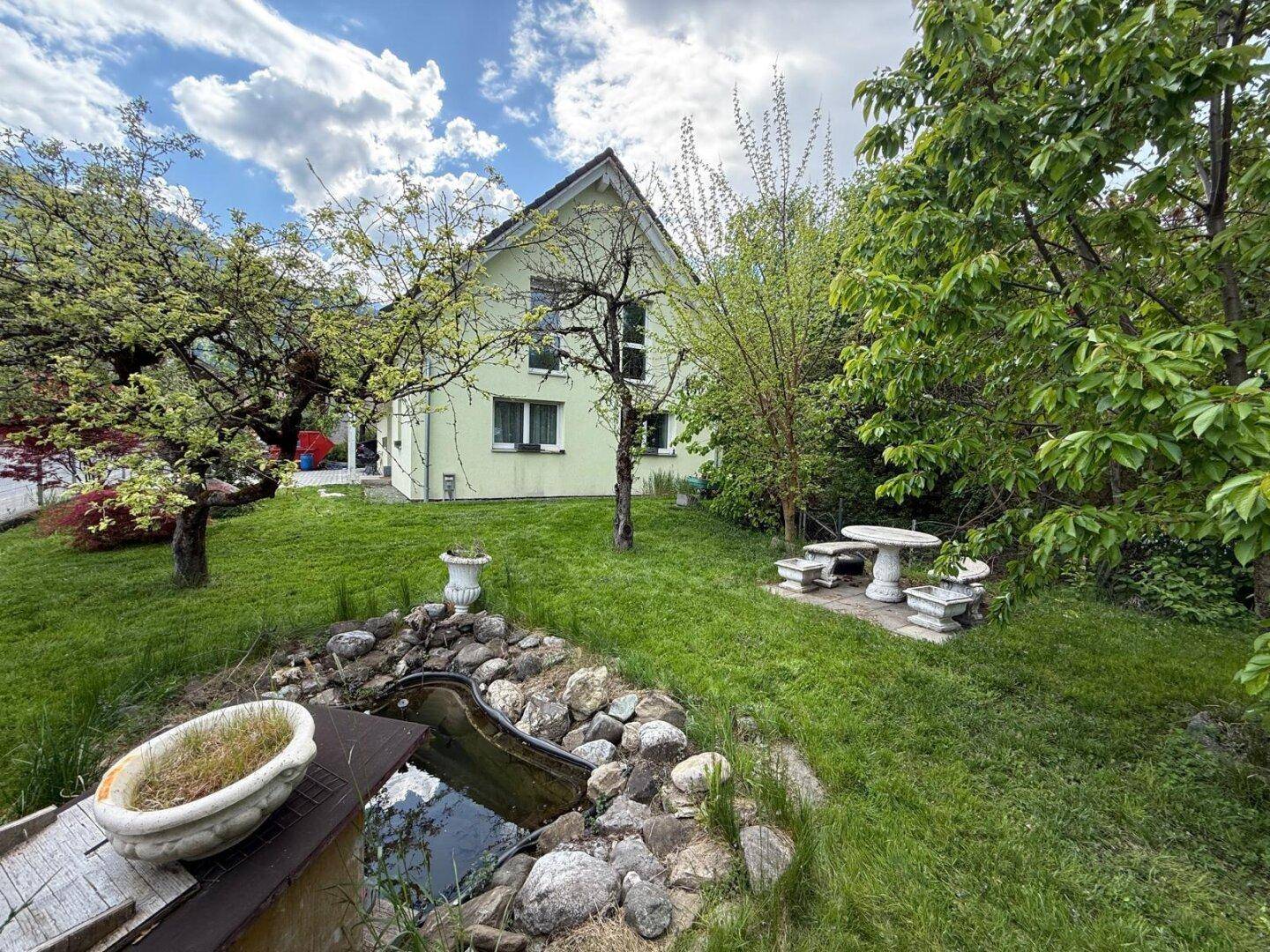 Hinterer Gartenbereich mit kleinem Teich, Steinsitzgruppe und viel Grünfläche.