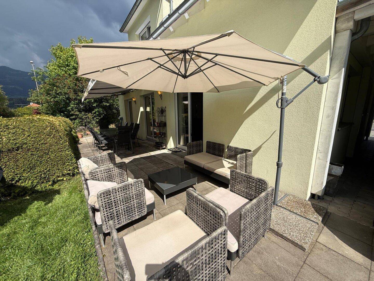 Gemütliche Terrasse mit bequemen Gartenmöbeln, Sonnenschirm und Blick ins Grüne.