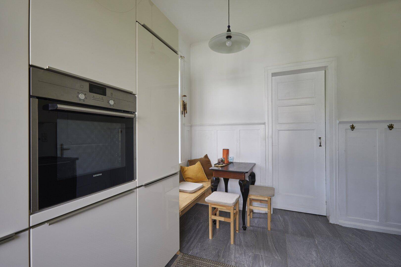 Moderne Küche mit hellen Einbauschränken, integriertem Backofen und kleinem Essbereich.