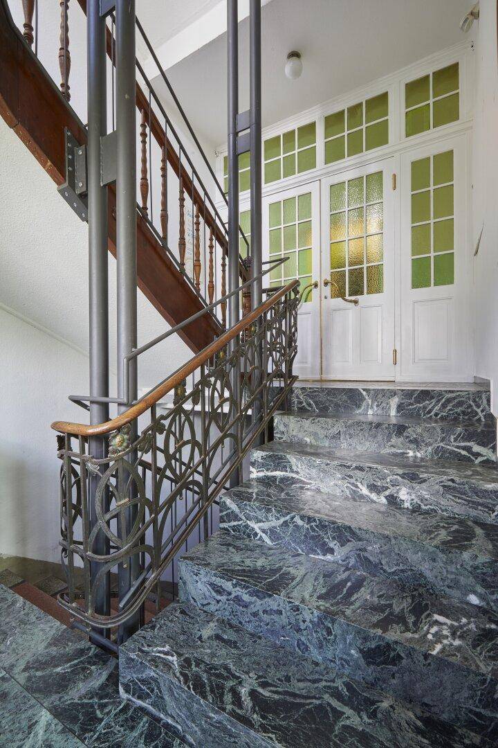 Elegantes Treppenhaus mit Marmorstufen, schmiedeeisernem Geländer und integriertem Aufzug.