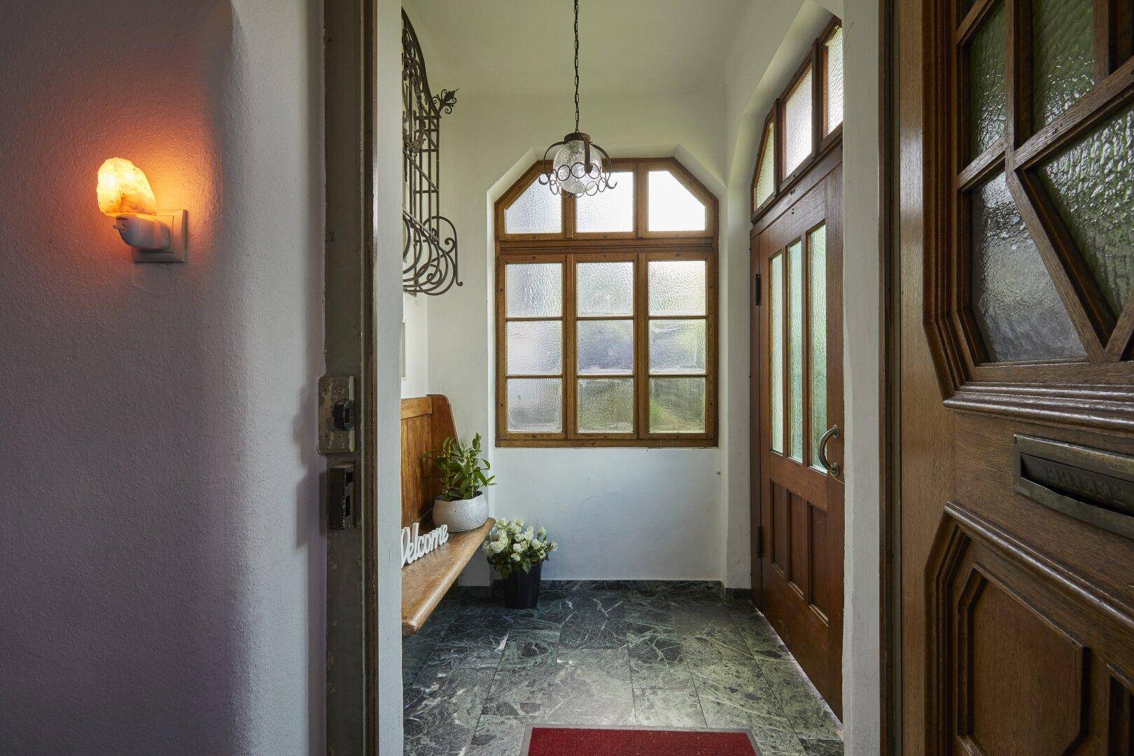 Eingangsbereich mit dunklem Marmorboden, Holztür und einem Fenster mit Sprossen.