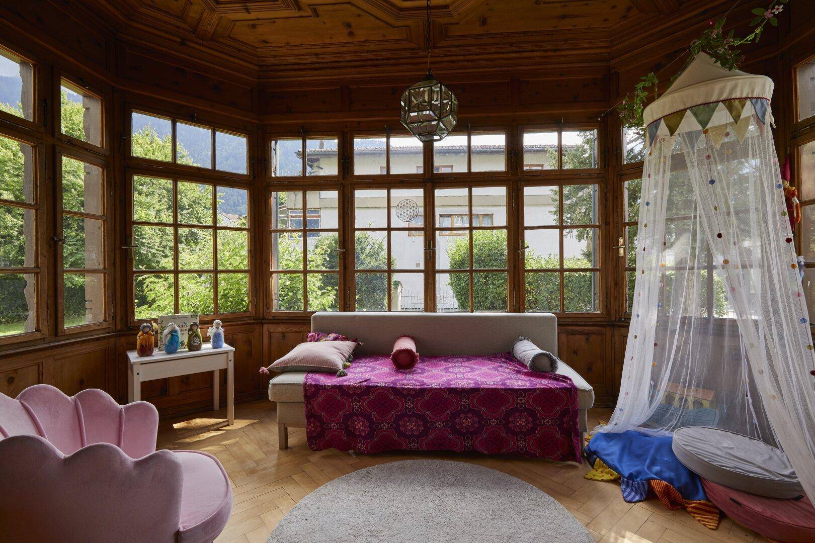Lichtdurchfluteter Wintergarten mit Holzvertäfelung, großen Fenstern und einer gemütlichen Sitzecke.