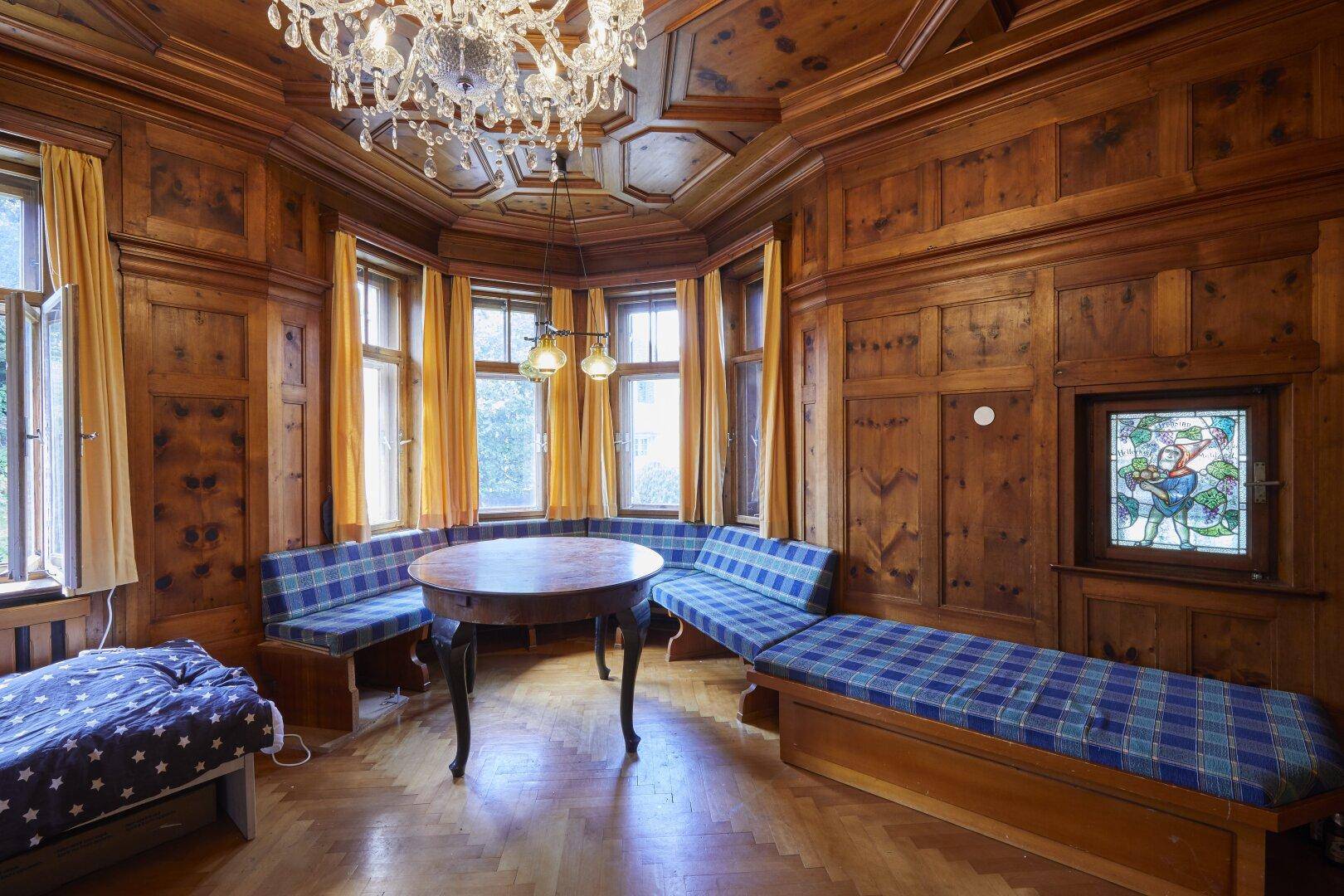 Gemütlicher Wohnbereich mit Holzvertäfelung, Erkerfenstern, Sitzbänken und einem Kronleuchter.