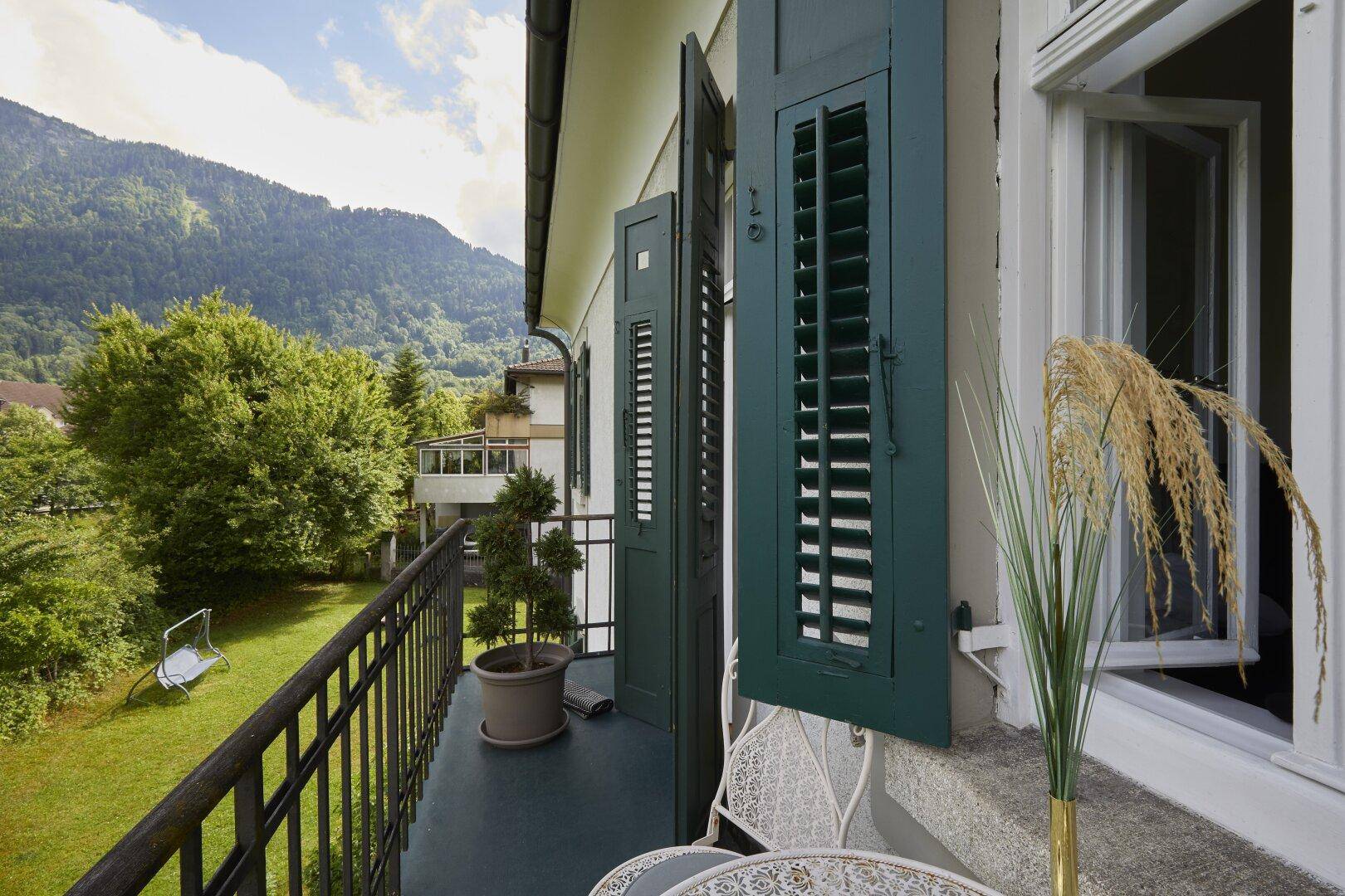 Kleiner Balkon mit schmiedeeisernem Geländer, Blick ins Grüne und auf die Berge.