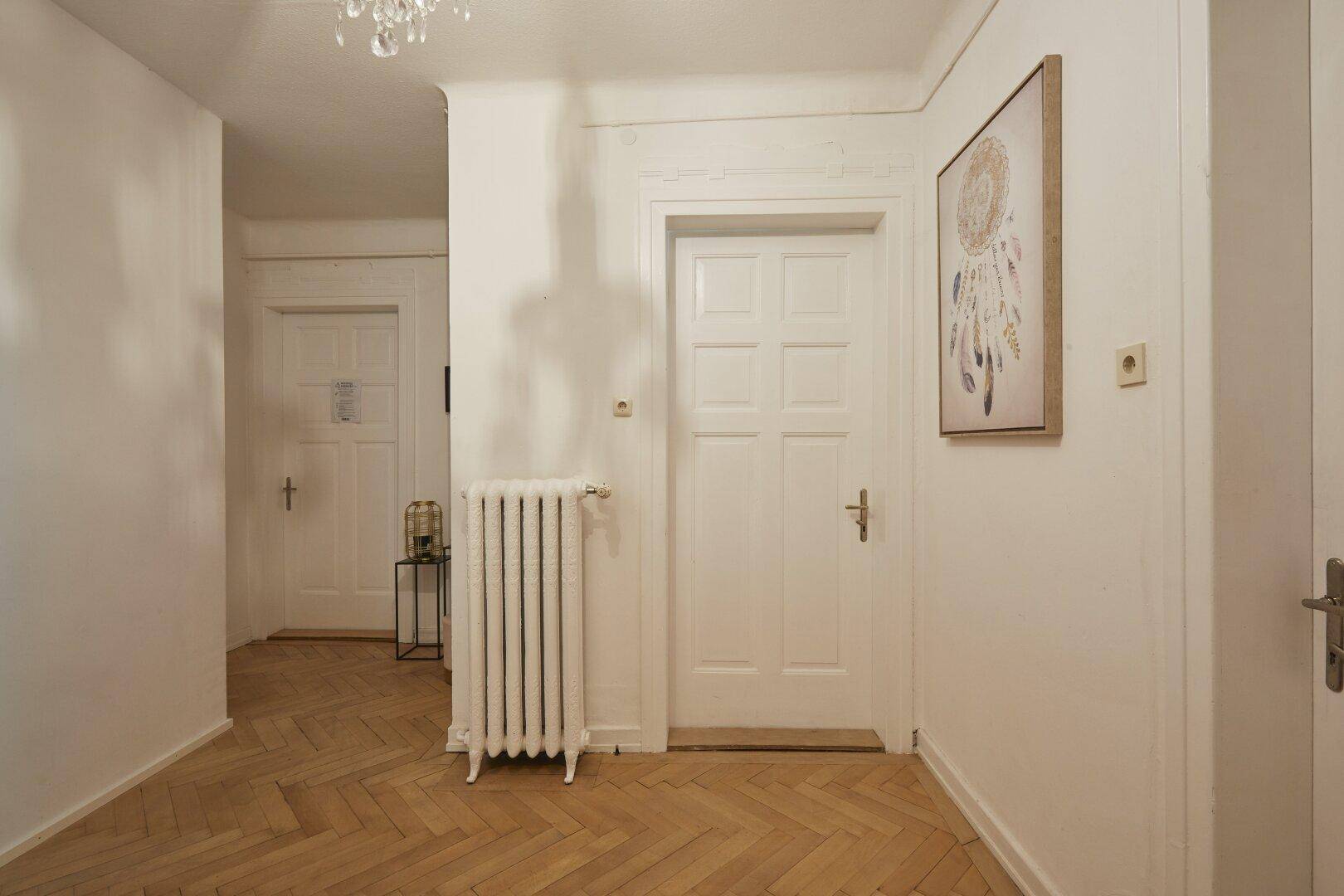Heller Flur mit Parkettboden, weißen Türen und einem klassischen Heizkörper.