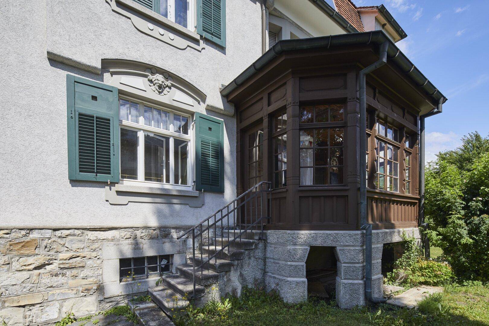 Detailansicht des hölzernen Eingangsbereichs mit Treppe und traditionellen Fenstern der historischen Villa.