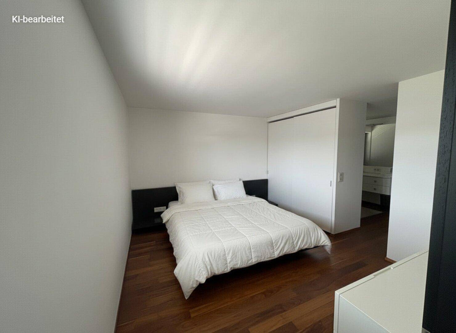 Schlafzimmer mit Doppelbett, dunklem Holzboden und weißen Wänden, inklusive Einbauschrank.