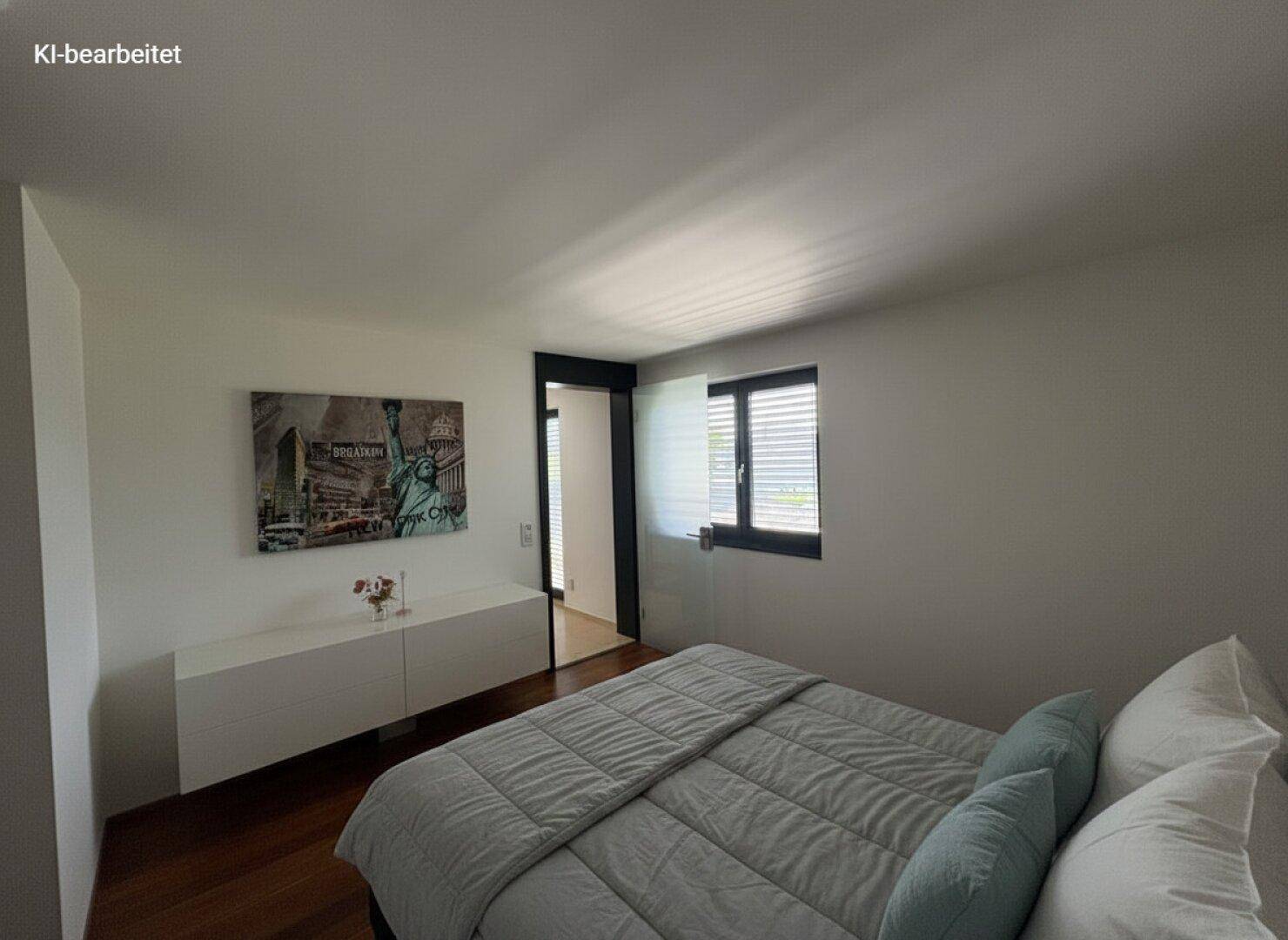 Schlafzimmer mit Bett, dunklem Holzboden und weißen Wänden, ein Fenster mit dunklen Jalousien.