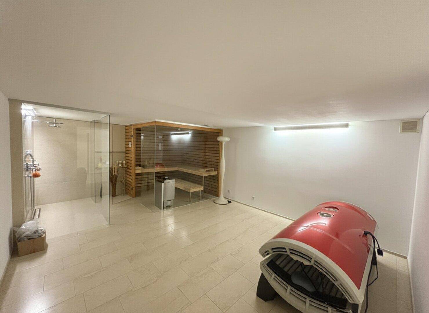 Wellnessbereich mit Sauna, begehbarer Dusche und Solarium, auf hellem Fliesenboden.