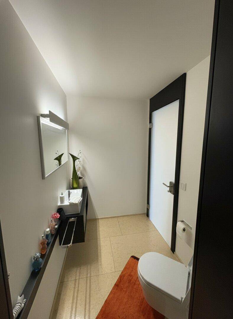 Gäste-WC mit wandhängendem WC, Einzelwaschbecken und hellem Fliesenboden.