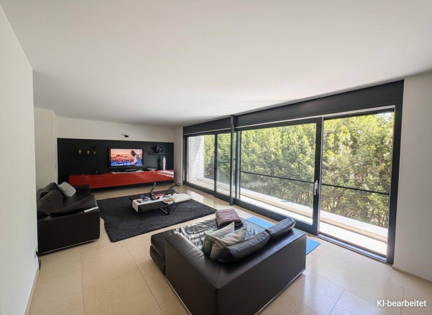 Helles Wohnzimmer mit großen bodentiefen Fenstern, dunklem Sofa und hellem Fliesenboden, mit Blick ins Grüne.