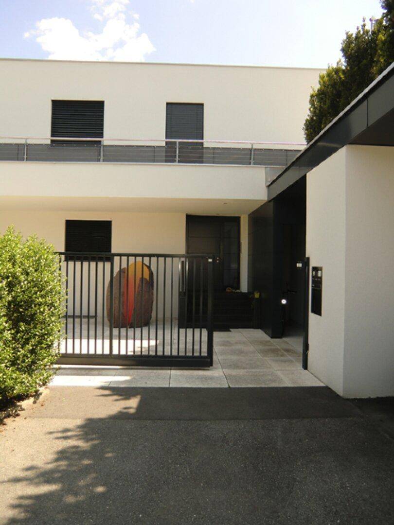 Moderner Eingangsbereich des Hauses mit schwarzem Tor, weißer Fassade und dunkler Eingangstür.
