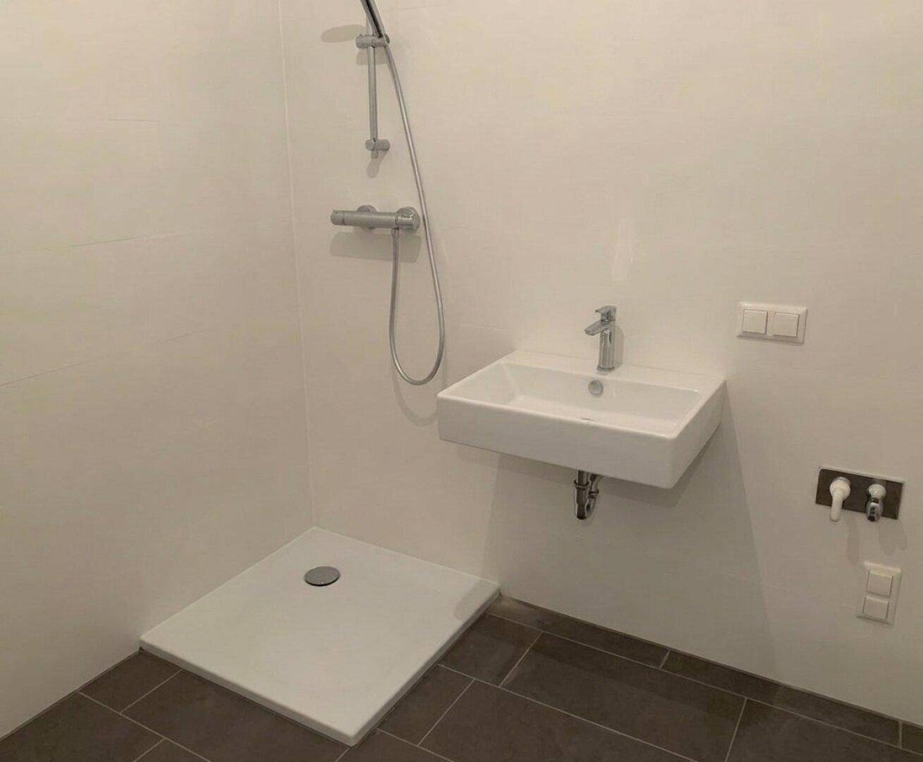 Modernes Badezimmer mit ebenerdiger Dusche, Wandwaschbecken und dunklen Bodenfliesen.