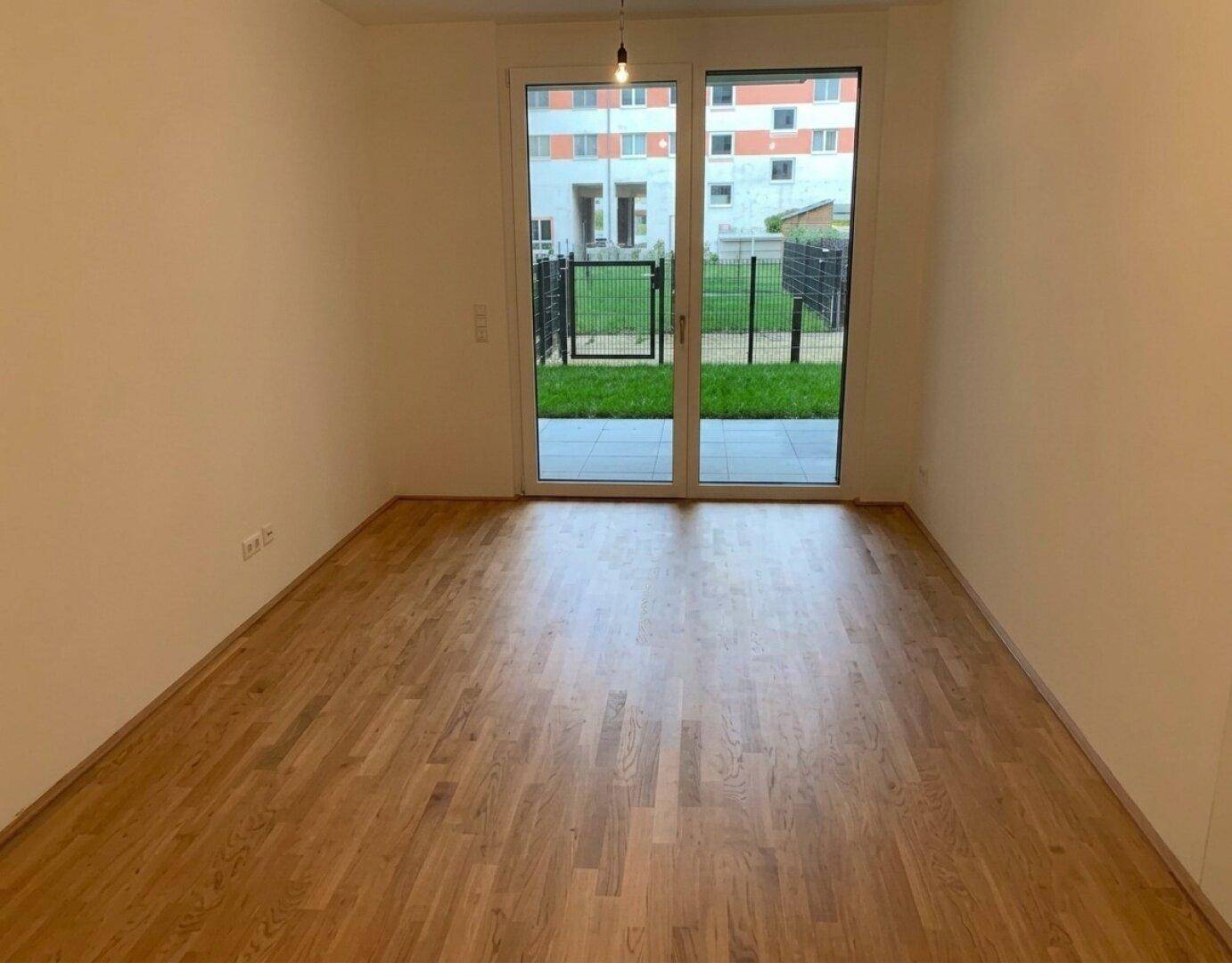 Geräumiger Wohnbereich mit hellem Parkettboden und Zugang zur Terrasse oder zum Garten.