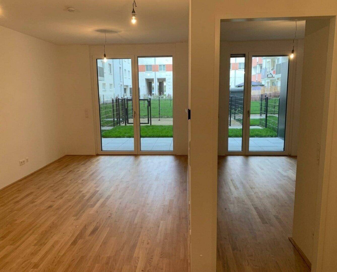 Heller Wohnraum mit Eichenparkettboden und großen Fenstern mit Blick ins Grüne.