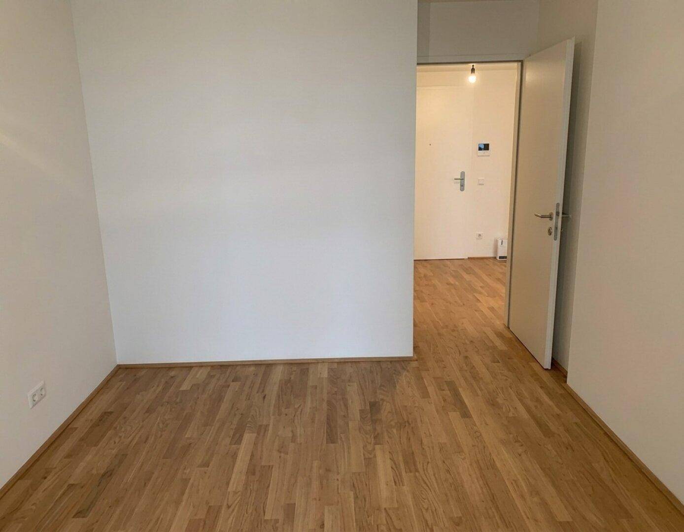 Leerer Raum mit hellem Parkettboden und weiß gestrichenen Wänden, bereit zum Einzug.
