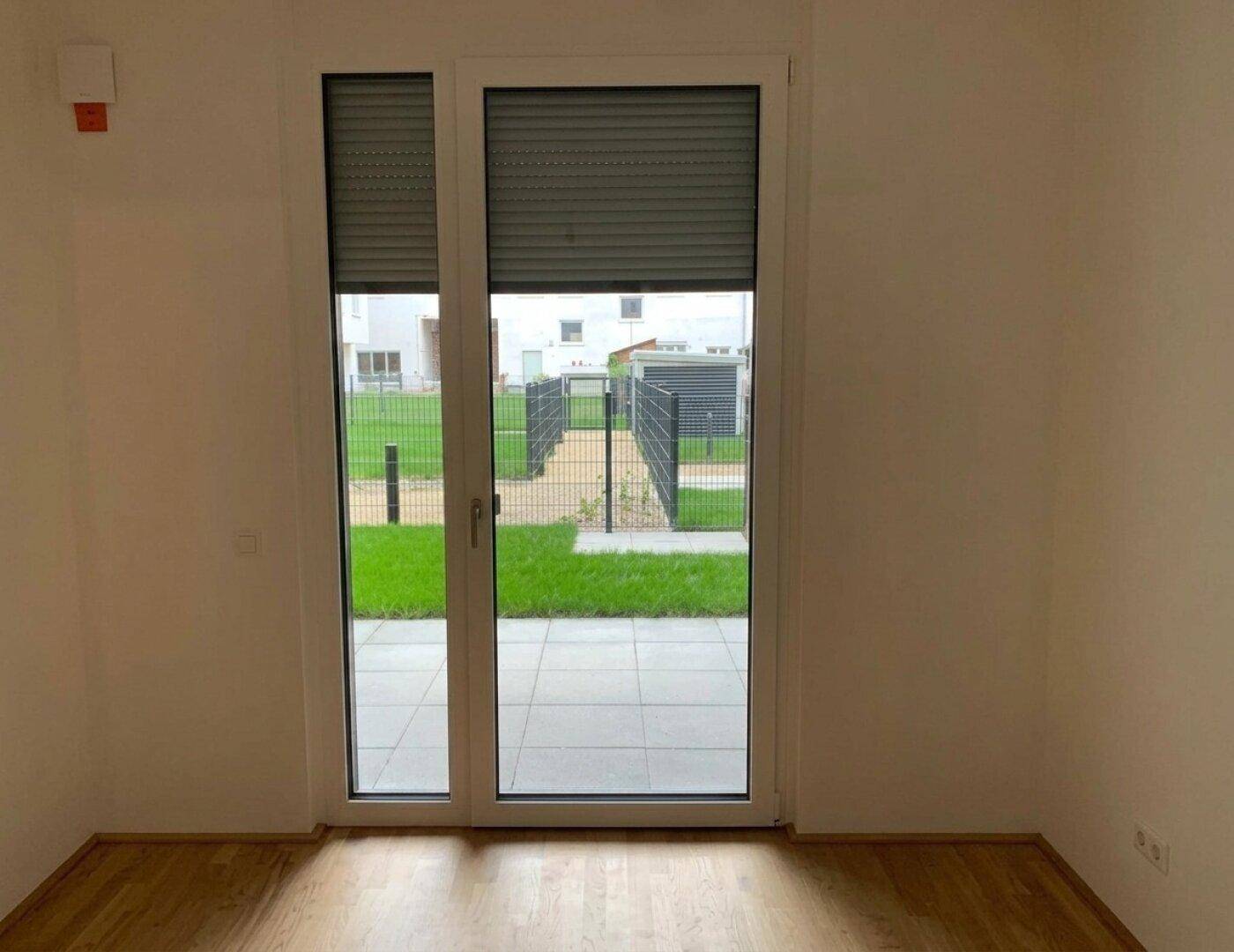 Heller Raum mit Parkettboden und Fenstertür, die den Blick auf den Außenbereich freigibt.