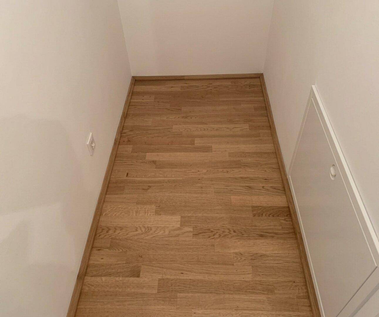 Schmaler Flur mit hellem Parkettboden und weiß gestrichenen Wänden, ideal für Stauraum.