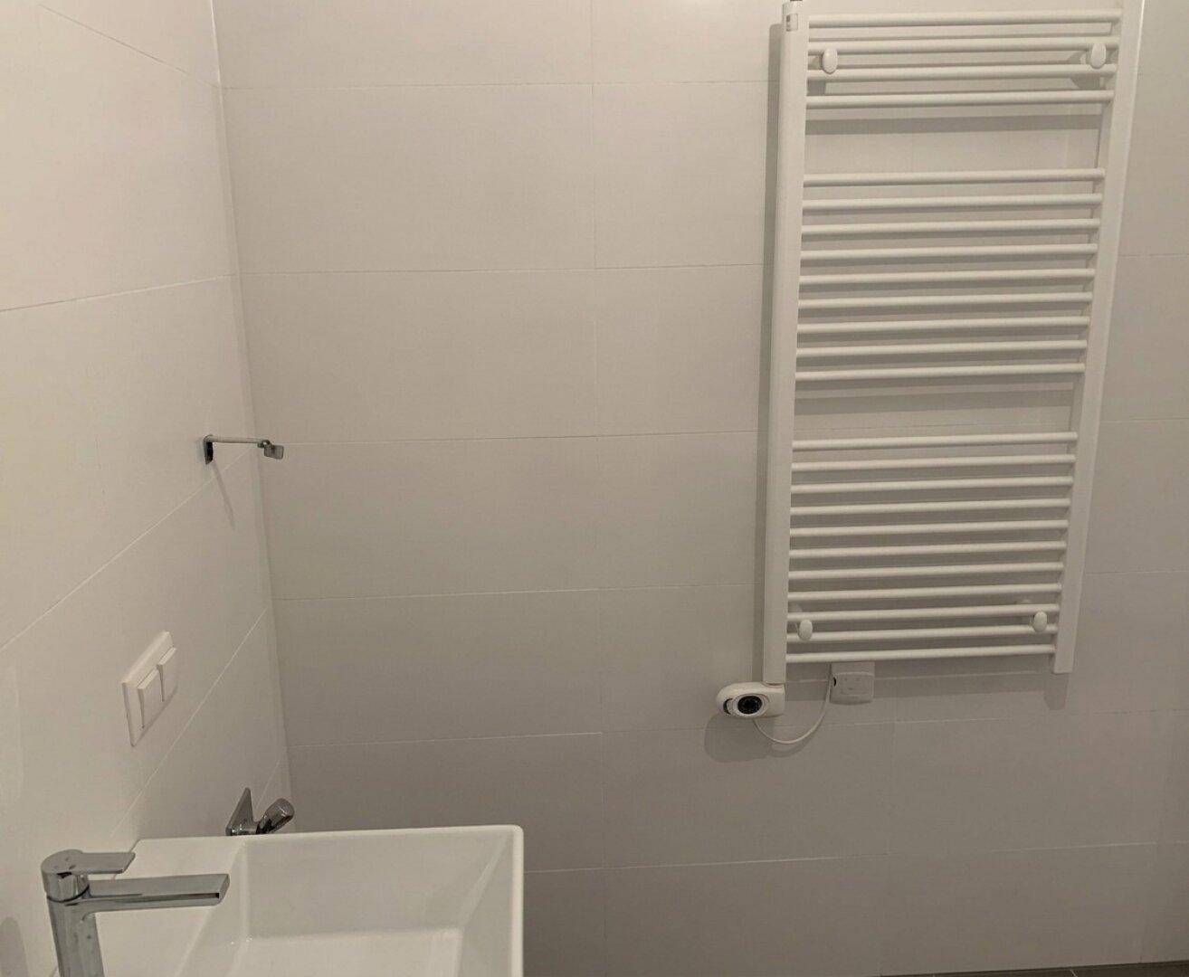 Badezimmer mit weißem Handtuchheizkörper und modernem Wandwaschbecken, hell gefliest.