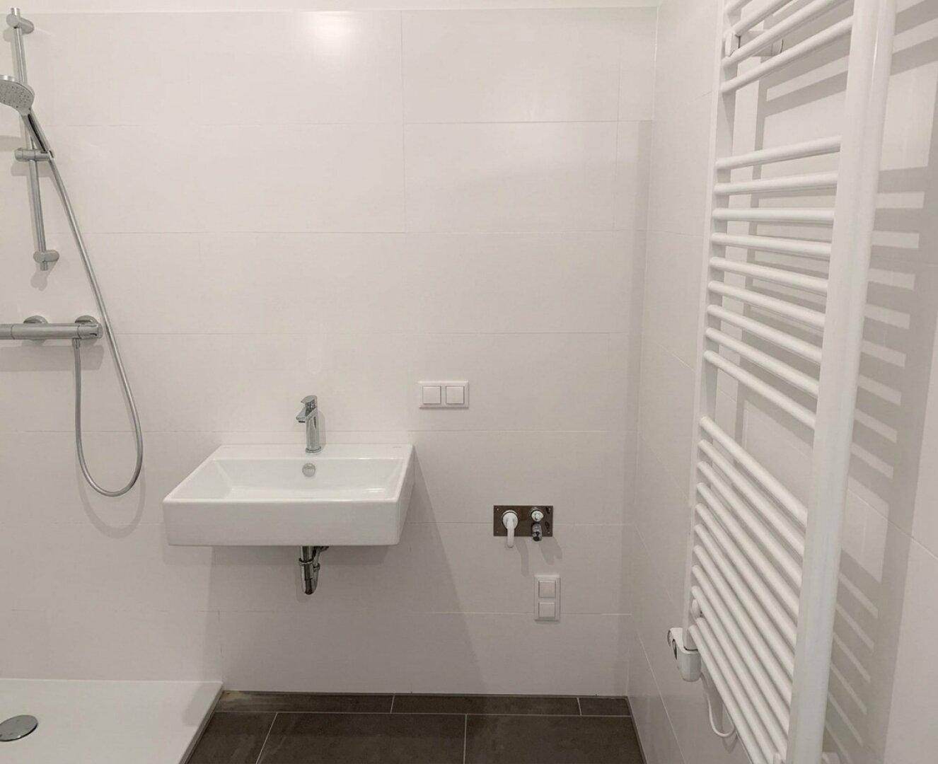 Helles Badezimmer mit Dusche, Wandwaschbecken und beheiztem Handtuchhalter, modern gefliest.